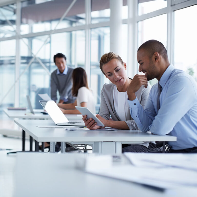 In a front two people discussing something on a tablet, blurry on an background other two discussing too, modern bright office environment.